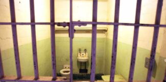 Interior of a prison cell with a toilet, sink, and metal bars