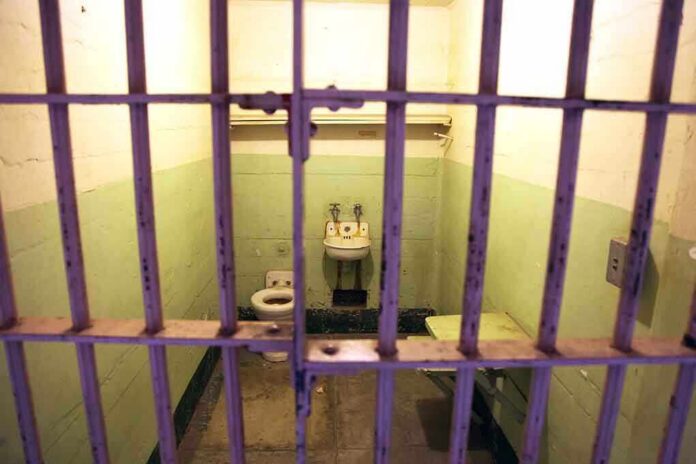 Interior of a prison cell with a toilet, sink, and metal bars
