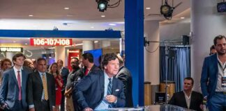News anchor at a studio desk with crowd and cameras in background