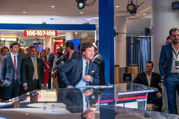 shutterstock_2251145707 News anchor at a studio desk with crowd and cameras in background