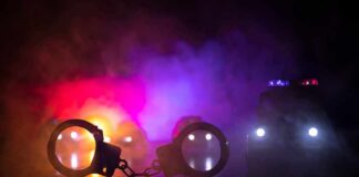 Handcuffs on a surface with police cars and flashing lights in smoky darkness