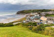 Emergency Powers Blitz As Surf Builds Coastal village by a wide sandy beach under cloudy skies