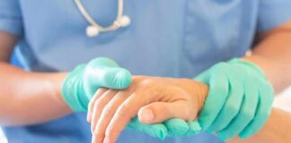 Healthcare worker in gloves holding a patient's hand
