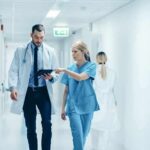 Your Doctor Didn’t Change—But Your Bill Did Doctors walking in a hospital corridor reviewing a tablet