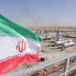 Iran flag over an oil and gas facility in a desert landscape
