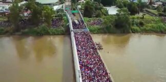 Crowd of people densely packed on a bridge over a muddy river