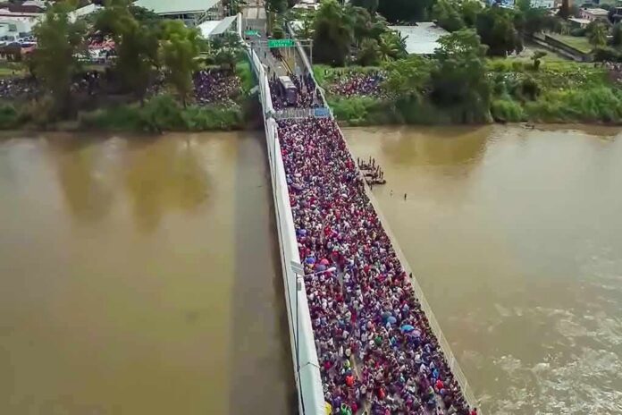 shutterstock_1229072224 Crowd of people densely packed on a bridge over a muddy river