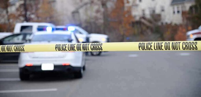 shutterstock_1230120343-1 Police tape cordons off a street with patrol cars and flashing lights in the background