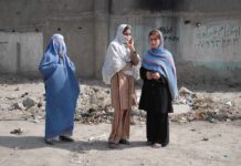 Three women in traditional attire standing in an urban setting with debris in the background