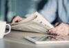 Fact-Check Torches Viral Migrant Claim Hands holding a newspaper beside a tablet and coffee mug