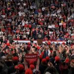 Early Votes Banked—Whose Power Play? Speaker at podium addressing large crowd in arena
