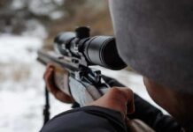 person aiming a rifle with a scope outdoors