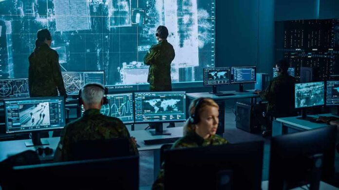 shutterstock_1936992886 Military analysts monitor data on multiple screens in a command center