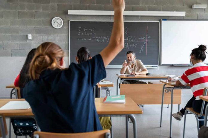 shutterstock_2014812635 Student raising hand in classroom during lesson