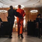 Ohio Court Melee: Throat Punch, Bones Broken Prisoner in orange jumpsuit escorted by officer in a courtroom