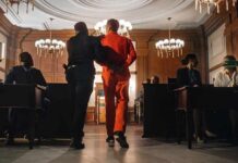 Prisoner in orange jumpsuit escorted by officer in a courtroom