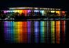 Modern building lit in rainbow colors reflected on water at night
