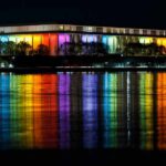 Federal Ruling Freezes Trump Plaza Plan Modern building lit in rainbow colors reflected on water at night