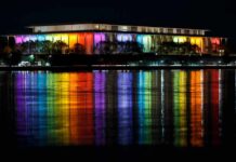 Federal Ruling Freezes Trump Plaza Plan Modern building lit in rainbow colors reflected on water at night