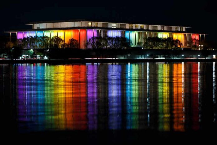shutterstock_2121991766 Modern building lit in rainbow colors reflected on water at night