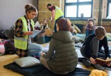 Volunteers assist people resting on mats in a temporary shelter