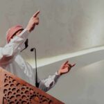 Mayor’s Ramadan Push Sparks Constitutional Fight Speaker in traditional attire gesturing from a carved wooden podium