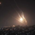 Night sky above a city with multiple rockets arcing and bright explosions