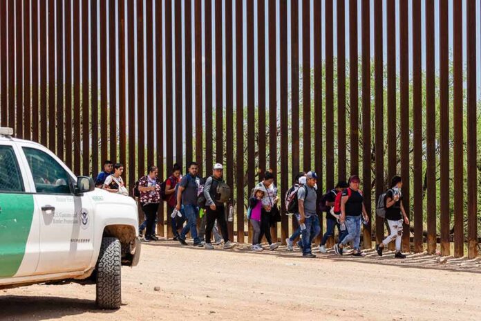 Group of people walking along a tall border fence beside a patrol vehicle