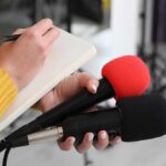 Sovereignty Wins A High-Stakes Island Showdown Journalist holding two microphones while writing in a notebook