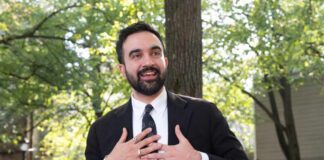 man in a suit speaking outdoors with hands on chest