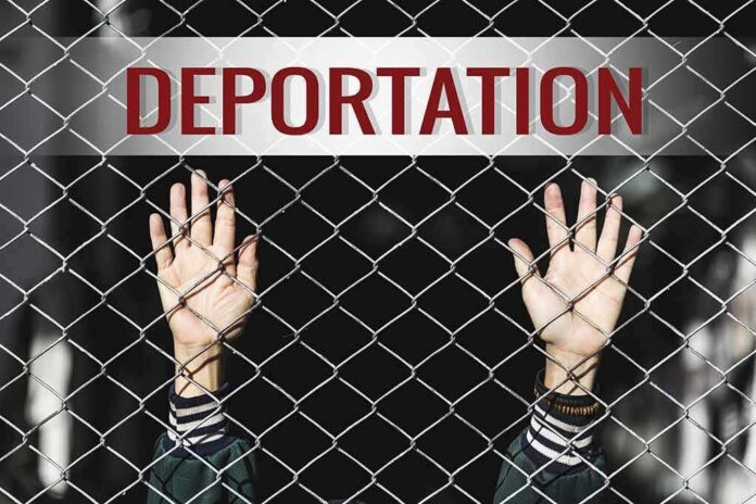 shutterstock_519187753 Hands gripping chain-link fence with deportation sign