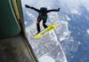 Skydiver jumps from plane with a skysurf board over snowy landscape