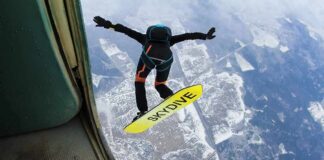 Skydiver jumps from plane with a skysurf board over snowy landscape