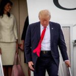 man in suit with red tie walking down airplane stairs