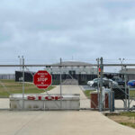 Undercover ‘Child’ Lures Navy Boss Chain-link fence with Restricted Area Stop No Photography sign.