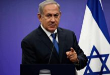Tense Ballots, Roaring Crowd In Jerusalem man in suit speaking at a podium with an Israeli flag