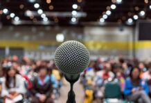 Neck Jab Sparks Outrage At TPUSA Event Microphone on stage facing a blurred audience