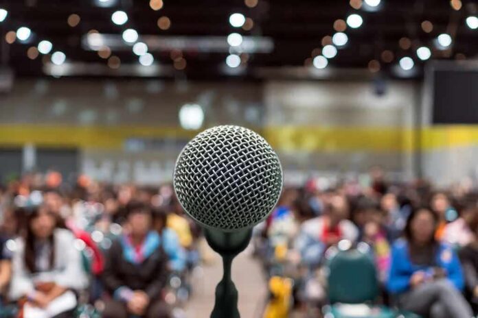 shutterstock_1079876627 Microphone on stage facing a blurred audience