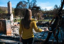 Woman in yellow sweater surveys burned ruins outdoors