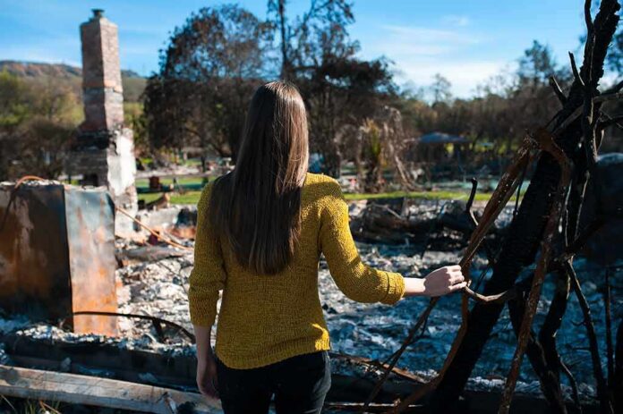 shutterstock_1141486334 Woman in yellow sweater surveys burned ruins outdoors