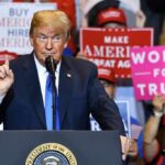 Massive Crowd, One Blunt Demand Donald Trump speaking at a rally podium with crowd holding signs