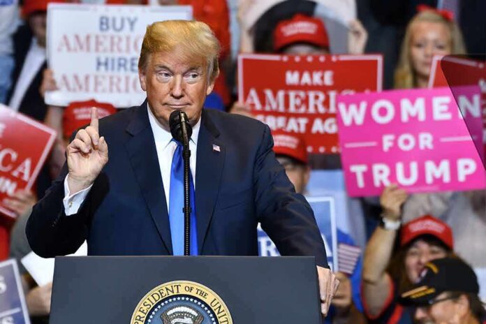 shutterstock_1148319797 Donald Trump speaking at a rally podium with crowd holding signs