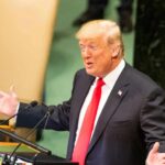 Donald Trump speaking at a podium with arms outstretched