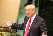 Crowd Roars, Press Fumes At WNBA Crack Donald Trump speaking at a podium with arms outstretched