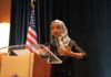 Ilhan Omar’s Home is Raided by Feds! Ilhan Omar speaking at a podium with a microphone