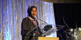Ilhan Omar speaking at a podium on a decorated stage