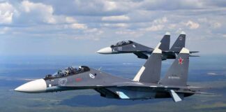 Two fighter jets flying in formation over landscape