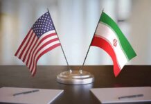 Foreign Guard Meddles – Targets Trump Voters United States and Iran desk flags on a stand