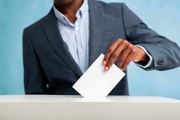 shutterstock_1696383901 Person in suit casting a ballot into a box