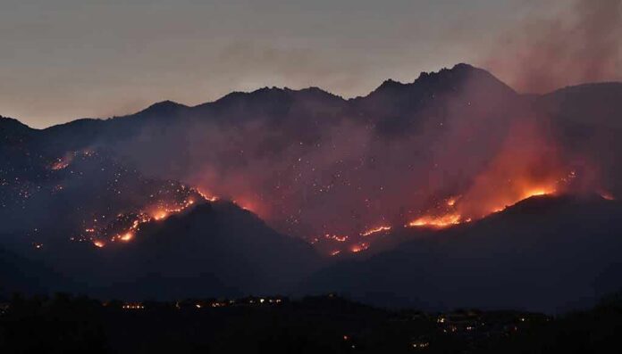 Wildfire burning along mountain slopes at dusk